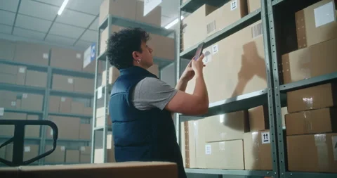 Male inventory manager scans code on parcel using smartphone, loads on pallet Stock Footage 307580794