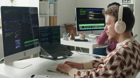 Male IT Engineer in Headset Coding on Computer next to Colleague in Office Stock Footage 330125417