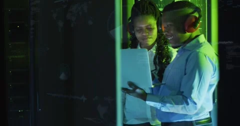 Male IT tech opening laptop and gesturing while female tech reviewing server Stock Footage 333965417