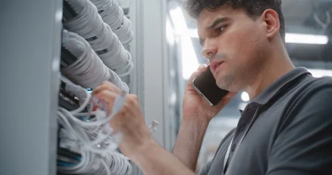 Male IT Technician Checking Rack Cabling During Smartphone Conversation Stock Footage 344974368