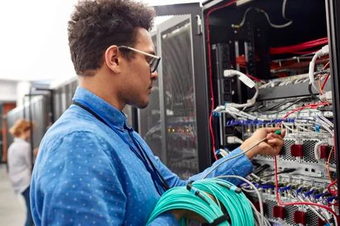 Male IT technician plugging cable into panel in server room Foto stock