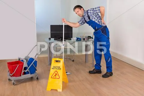 Male Janitor Suffering From Back Pain While Mopping In Office Stock Photos