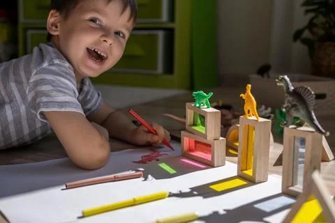 Male kid playing wooden bricks and dinosaurs drawing shadow on paper early Stock Photos