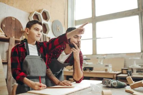 Male kid pointing at something and craftsman looks at it at workshop Stock Photos