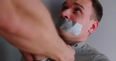Male kidnapper torturing his scared abuse man victim with tied mouth on gray 動画素材 304866499