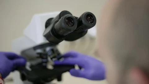 Male laboratory assistant looks through a microscope and analyzes Stock Footage 75907569
