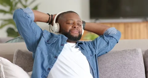 Male leaning back, settling on sofa wearing headphones, closing eyes and Stock Footage 337026208