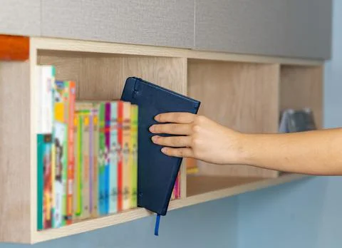 Male left hand choosing and picking blue book in home book shelf. Stock Photos