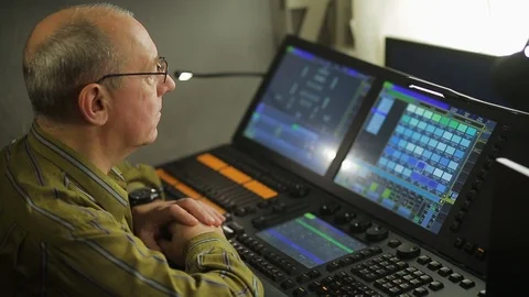 A male lighting programmer at a remote control programs the stage light for a Video stock 125909604
