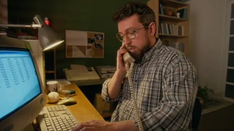 Male Manager Working on Vintage Computer while Talking on Corded Telephone Stock Footage 327241076