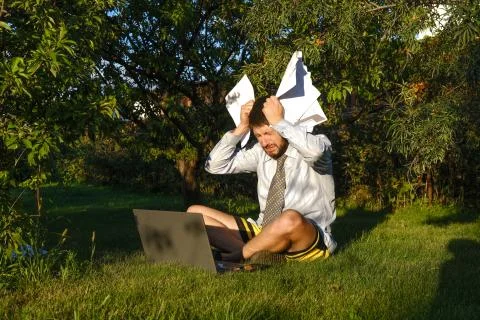 A male manager works remotely at home, makes reports. He is sitting on the lawn Stock Photos