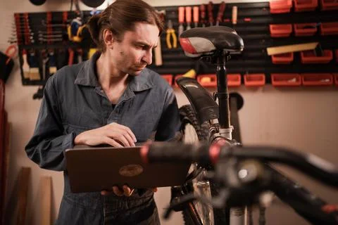 Male mechanic using laptop computer to check bicycle repair instructions whil Stock Photos
