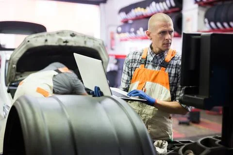 Male mechanic using laptop while repairing car in service Foto stock