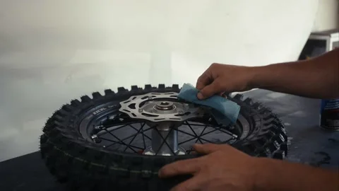 A Male mechanic using rag to clean dirt bike rim on garage top Stock Footage 155540481