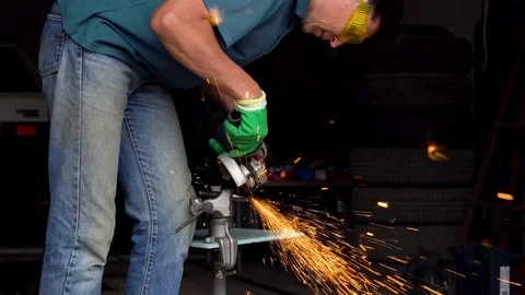 Male-middle-aged worker with angular grinding machine is cutting the metal Stock Footage 76987894