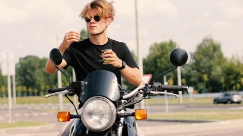 Male motorcyclist drinking coffee while sitting on a motorcycle in summer Stock Footage 248421404