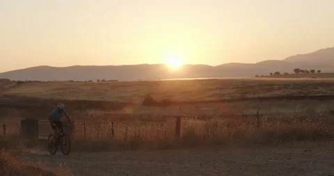 Male mountain biker speeding down a dirt road at sunrise Stock Footage 138096054