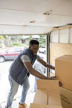 Male mover loading cardboard boxes into moving van Stock Photos