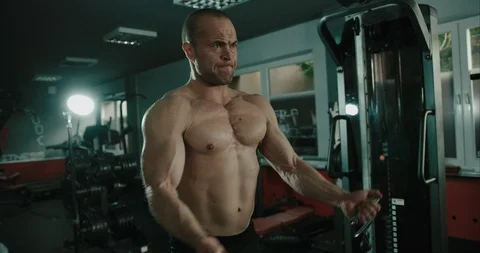 Male muscular bodybuilder is pulling on strings on workout machine to Stock Footage 123127353