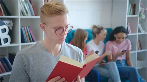 Male nerd is reading tutorial while teen girls are laughing behind his back Stock Footage 106437808