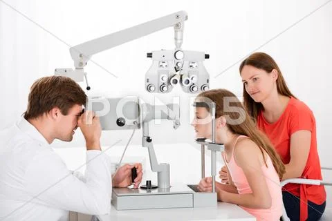 Male Optometrist Examining Eyesight Of Girl While Mother Sitting Beside Her