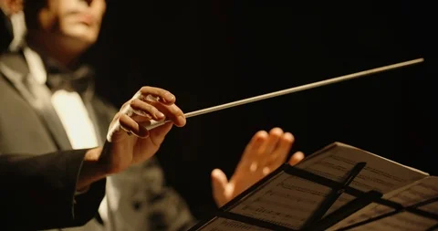 Male orchestra conductor controlling music in orchestra pit by movement of his Stock Footage