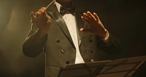 Male orchestra conductor wearing tux standing in front of music stand Stock Footage