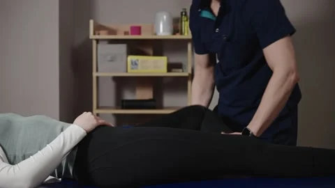A male osteopath performs physical therapy on a female patient. The doctor looks Stock Footage 283260520