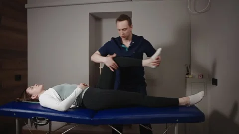A male osteopath performs physical therapy on a female patient. The doctor looks Stock Footage 284314960