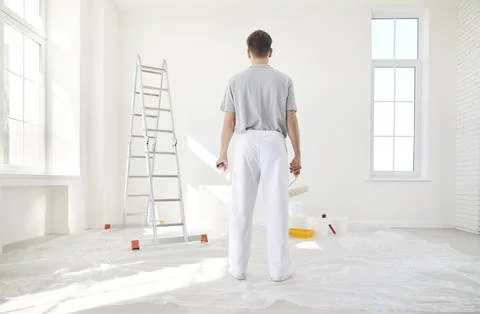 Male painter standing back in empty room holding a bucket and paint roller Stock Photos