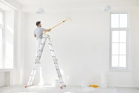 Male Painter Using Roller To Paint Wall During Home Renovation Stock Photos