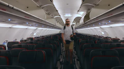 Male Passenger Walking Down Empty Airplane Aisle with Backpack and Hat. Stock Footage 338362659