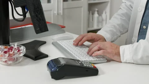 Male Pharmacist Typing on Computer at Pharmacy Counter Stock Footage 348060692