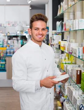 Male pharmacist wearing white coat standing in drug store Stock Photos