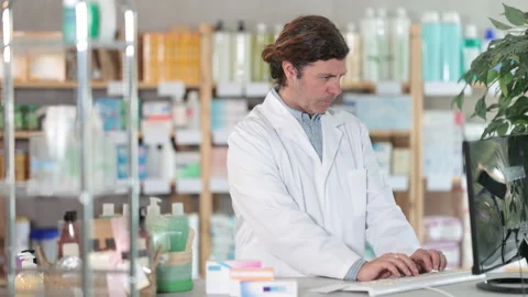 Male pharmacist working at computer in pharmacy Stock Footage 330041454