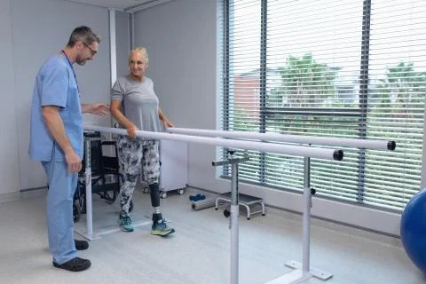 Male physiotherapist helping patient walk with parallel bars Stock Photos
