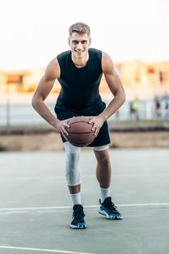 Male player posing while holding a basketball outdoors Stock Photos