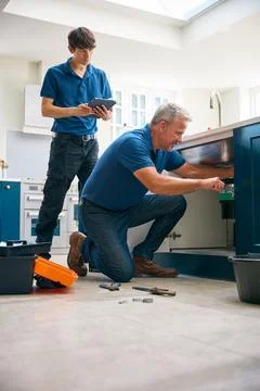Male Plumber With Trainee Using Digital Tablet Fixing Waste Disposal Unit I.. Stock Photos