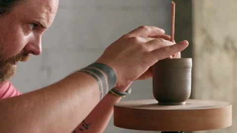 A male potter processes the edges of a clay teapot on a potter's wheel Stock Footage 145534582