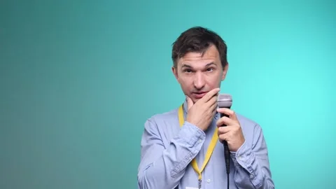 Male presenter holding a microphone, looking away and thoughtfully touching his Stock Footage 342766101