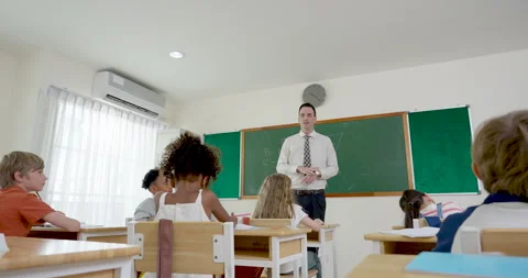 Male primary teacher leads math lesson from front of modern classroom while Stock Footage 341929638