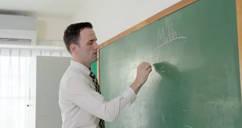 Male primary teacher writes math lesson notes on green chalkboard with chalk, Stock Footage 341930933