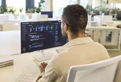 Male programmer coding at desktop computer in bright modern office workspace Stock Photos