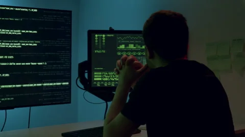 Male programmer, focused on multiple computer screens displaying code and data Stock Footage 314270699