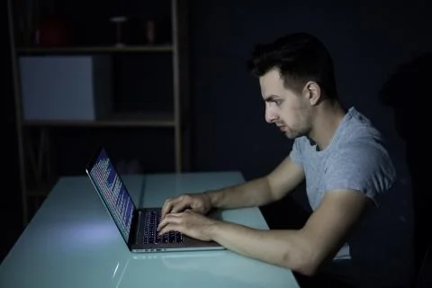 Male programmer working on desktop computer at white desk in office in dark 写真素材