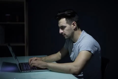 Male programmer working on desktop computer at white desk in office in dark 写真素材
