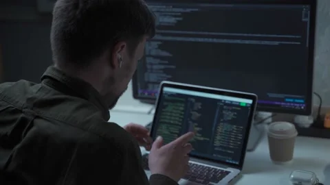 A male programmer works at a computer and uses an in-ear headset to talk with a Stock Footage 169530940