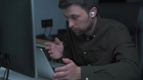 A male programmer works at a computer and uses an in-ear headset to talk with a Stock Footage 169531314