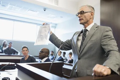 Male prosecutor attorney holding evidence bag at podium in legal trial courtroom Stock Photos