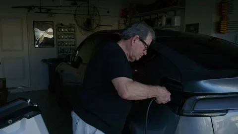Male pulls the plug of his home EV charger out and smiles at the camera Stockbeeldmateriaal 332996179